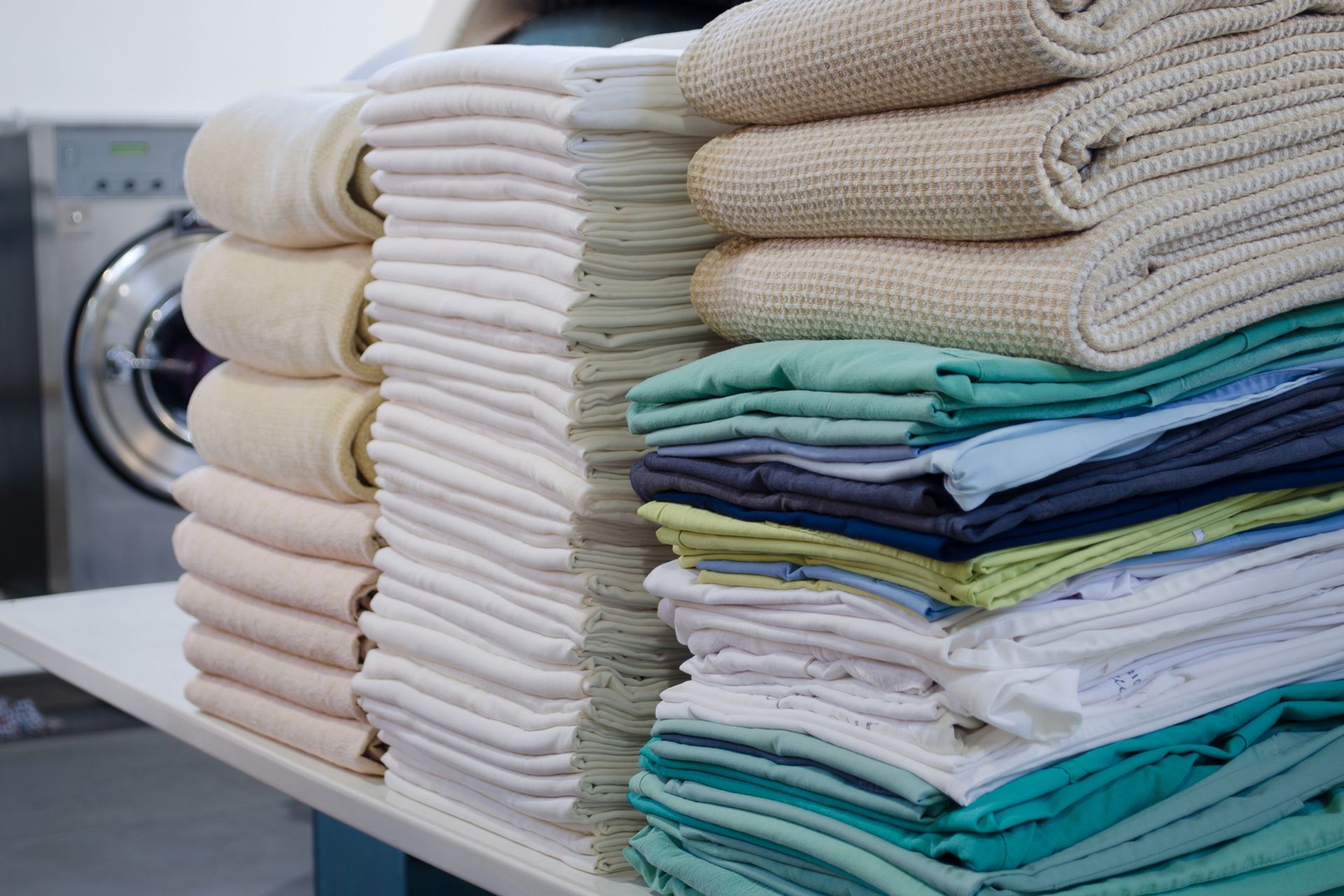 A stack of towels is sitting on a table in front of a washing machine.