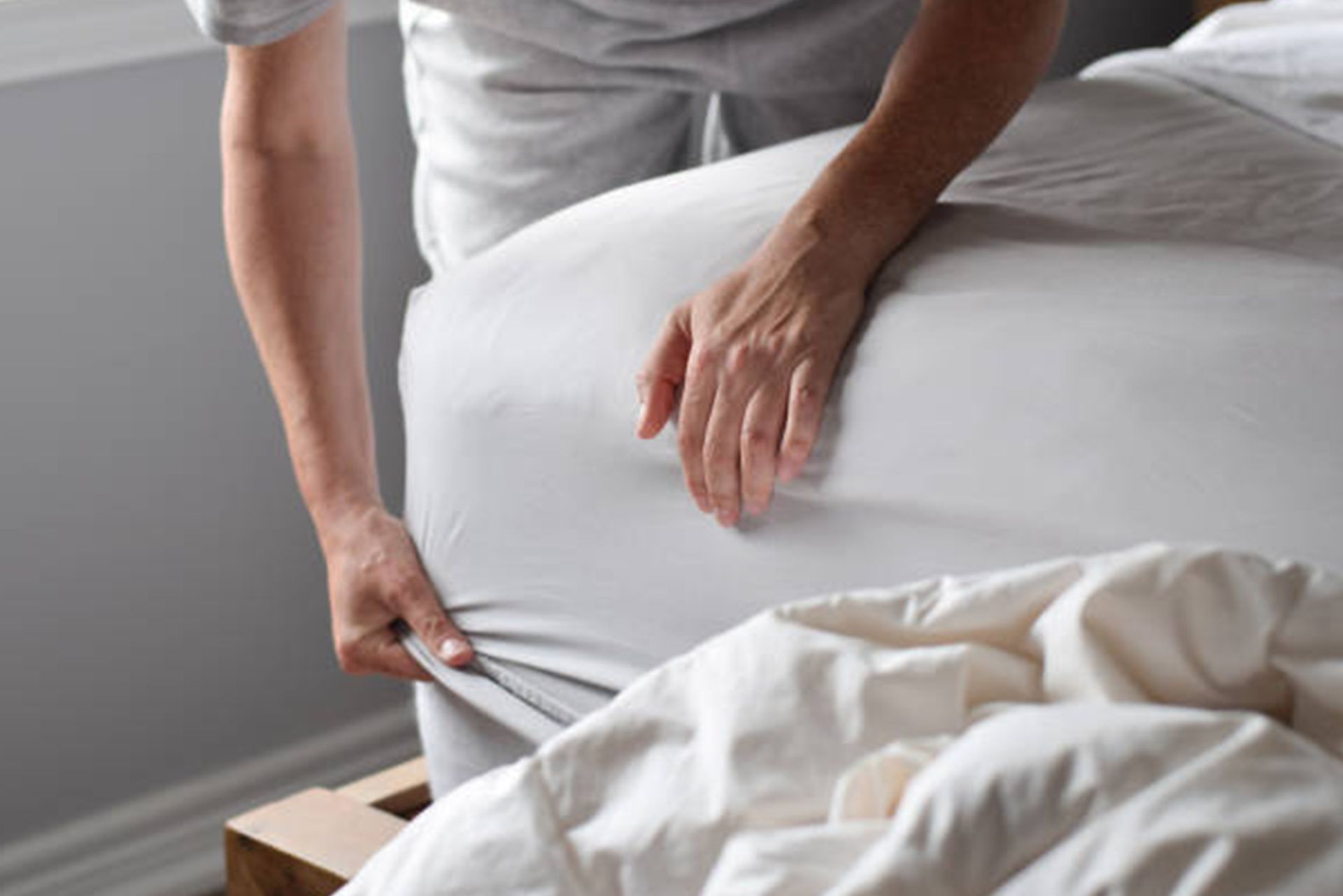 A person is putting a sheet on a bed.