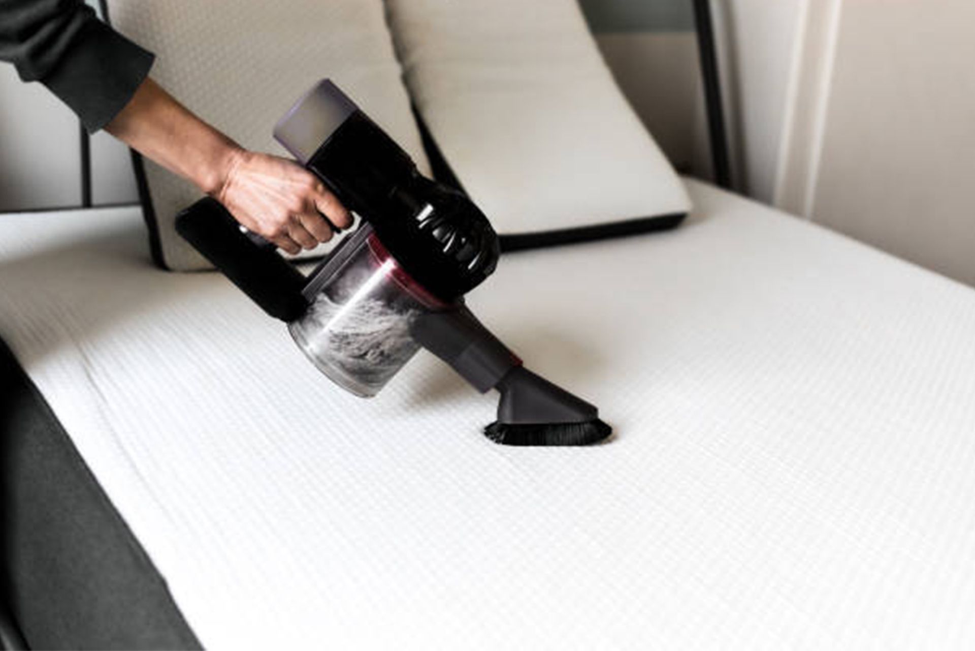 A person is cleaning a mattress with a vacuum cleaner.