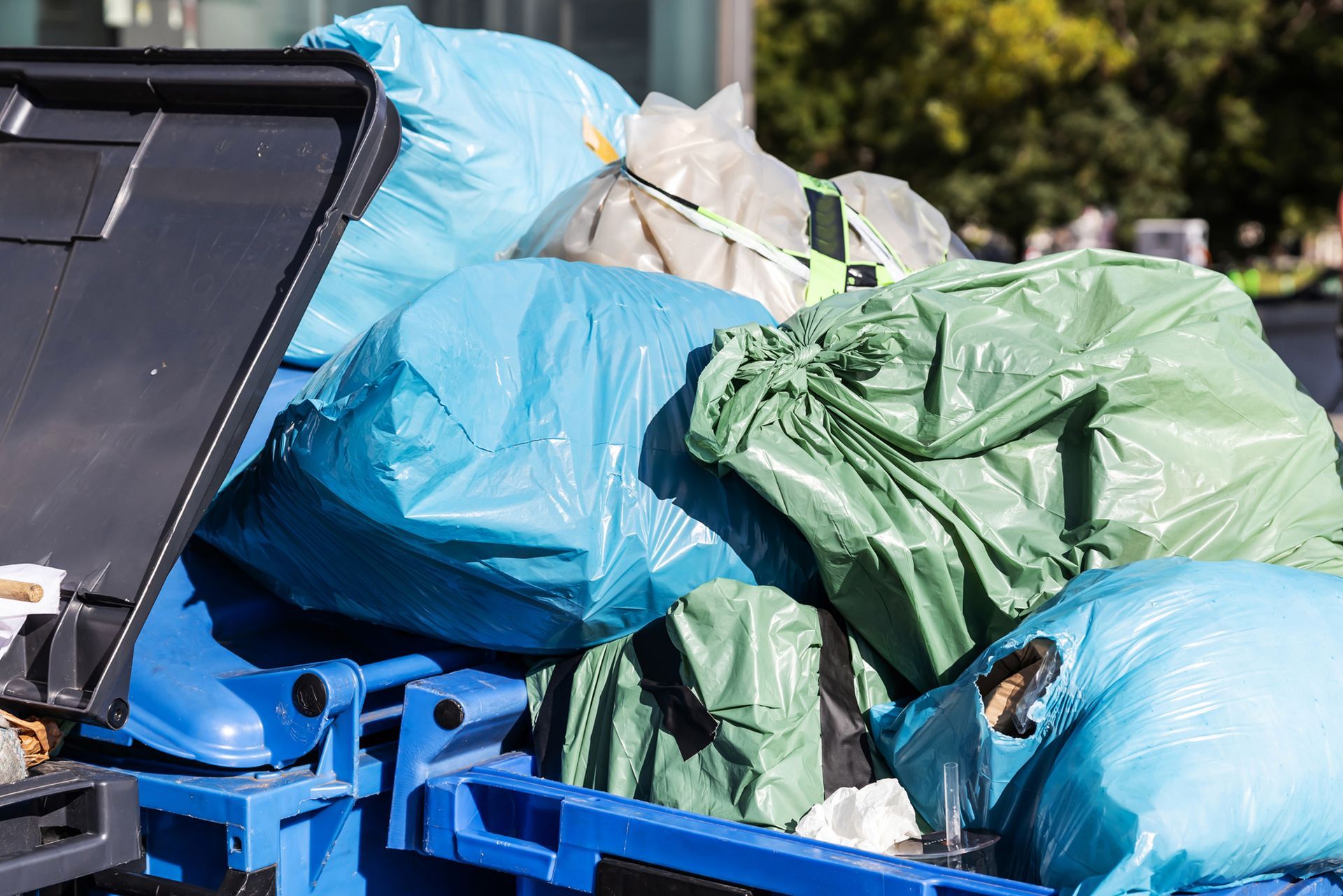 A blue dumpster filled with lots of garbage bags.