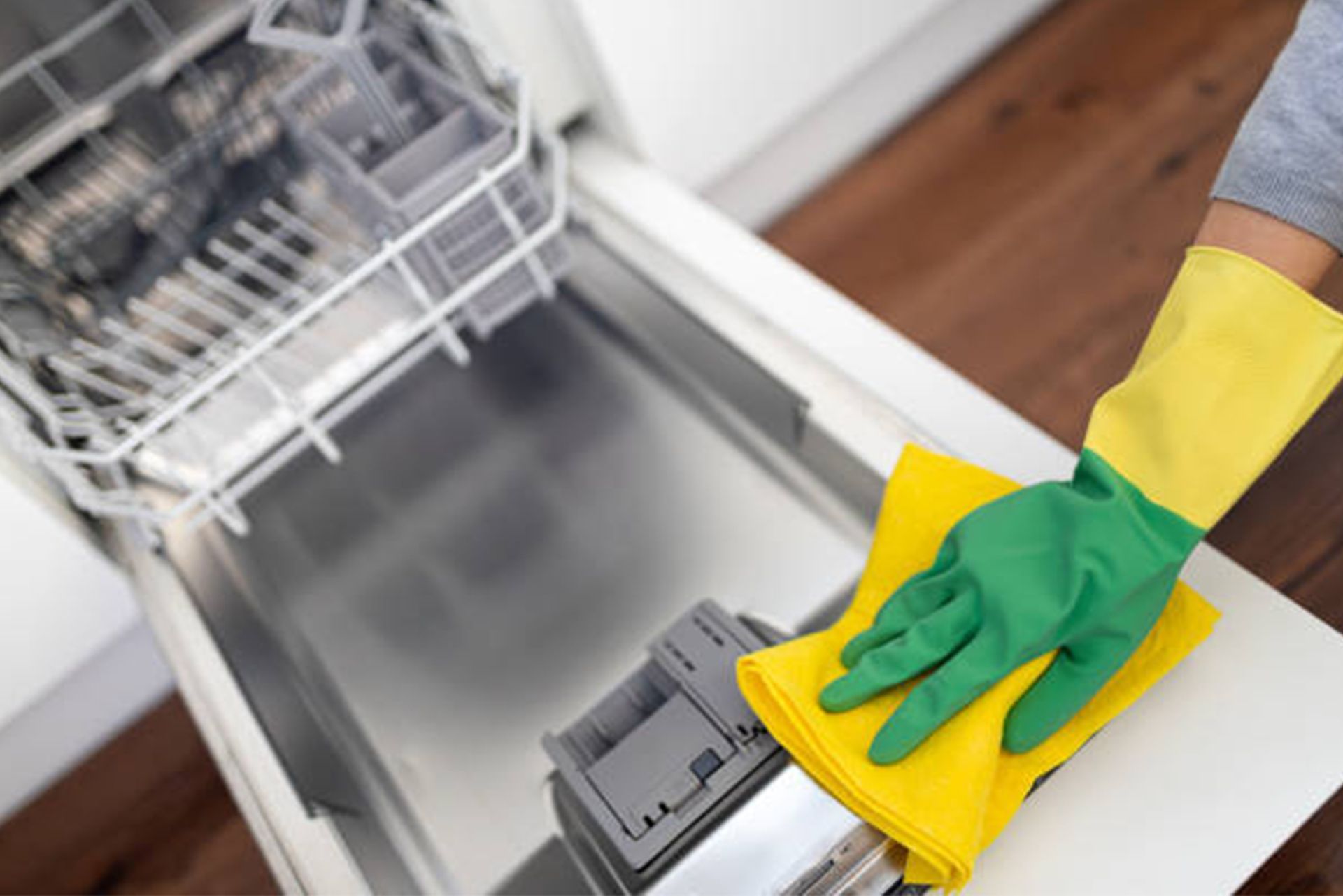 A person wearing green and yellow gloves is cleaning a dishwasher with a yellow cloth.