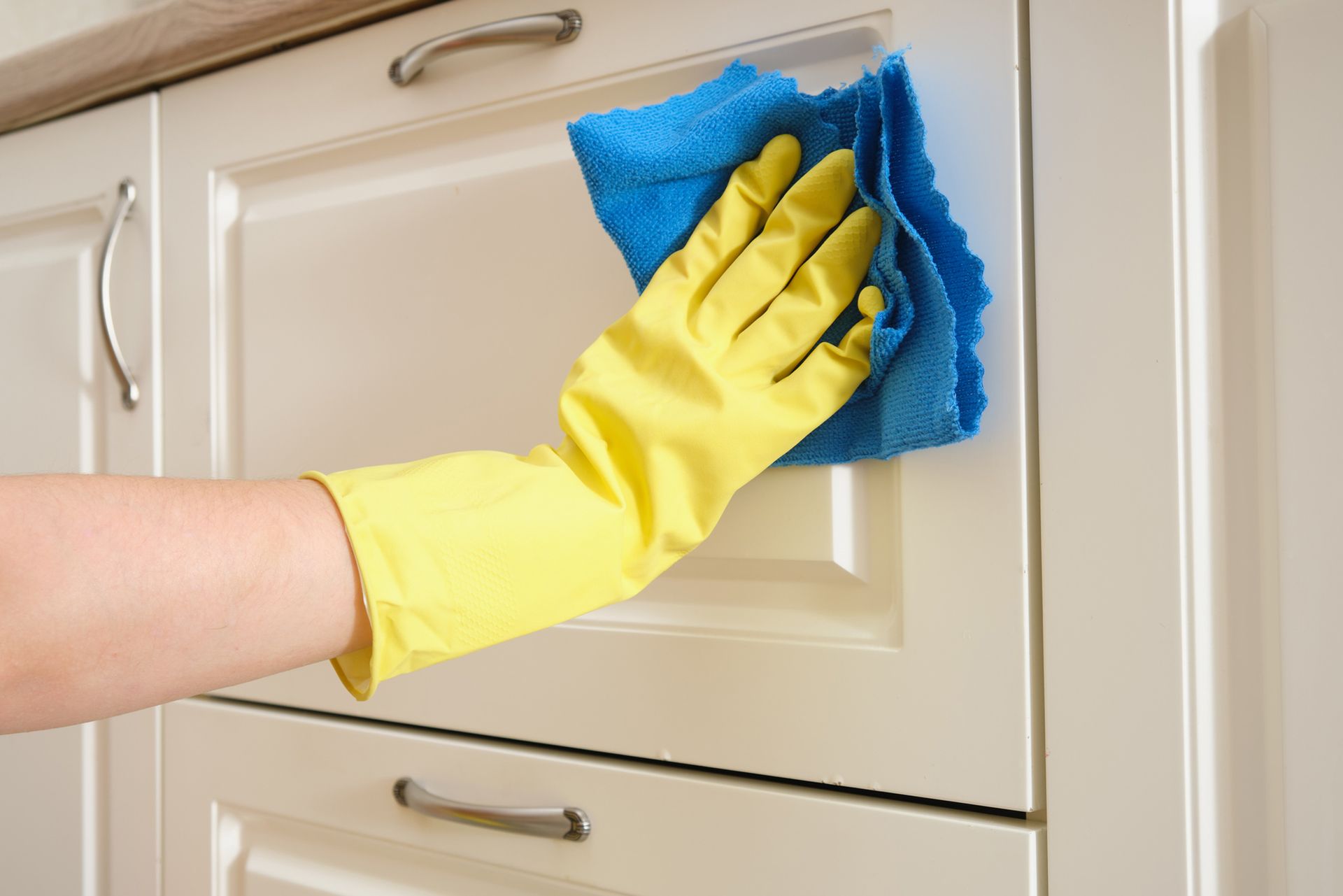 A person wearing yellow gloves is cleaning a cabinet with a cloth.