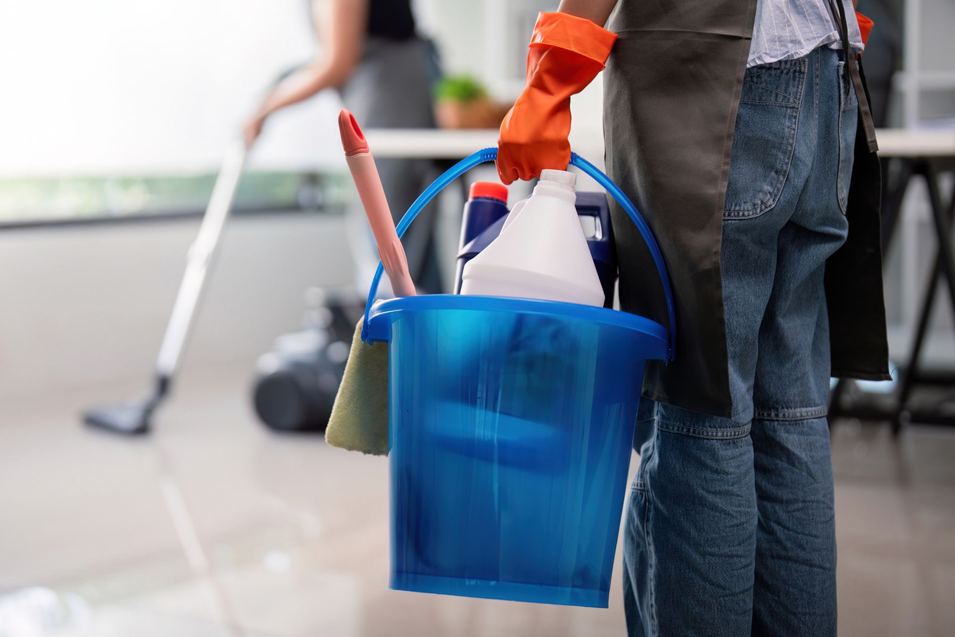 A person is holding a bucket of cleaning supplies.