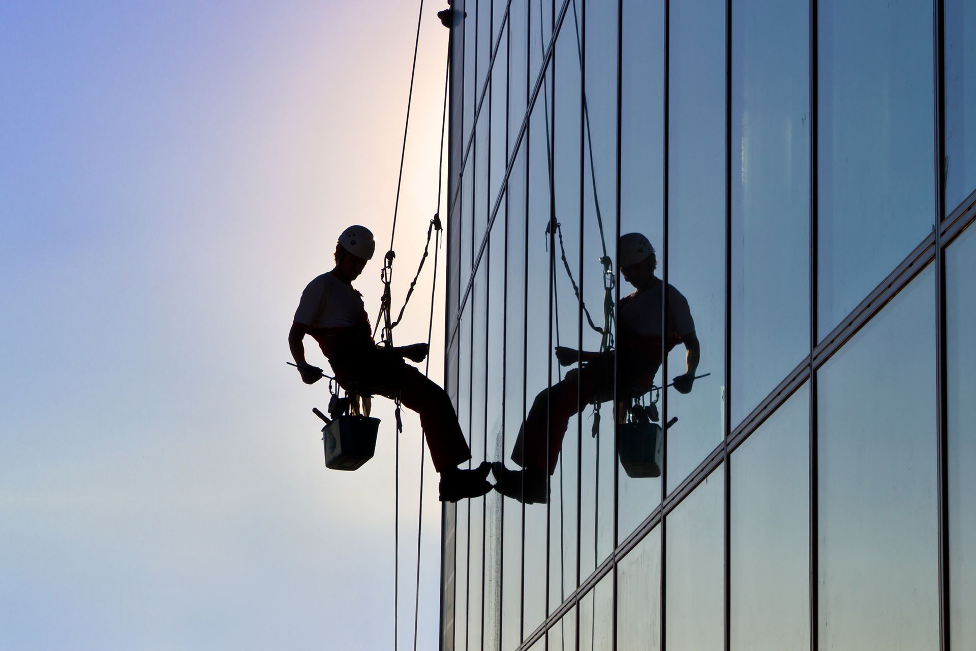 Two men are cleaning the windows of a tall building.