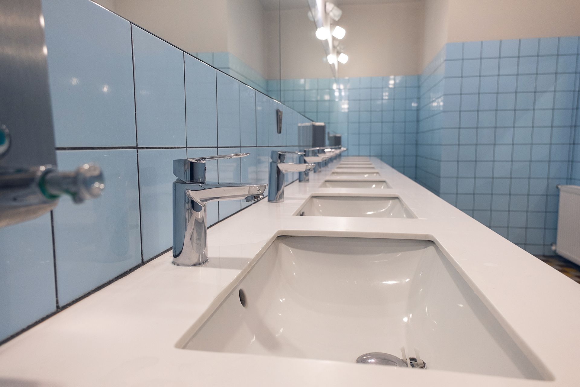 A row of sinks in a public restroom with blue tiles.