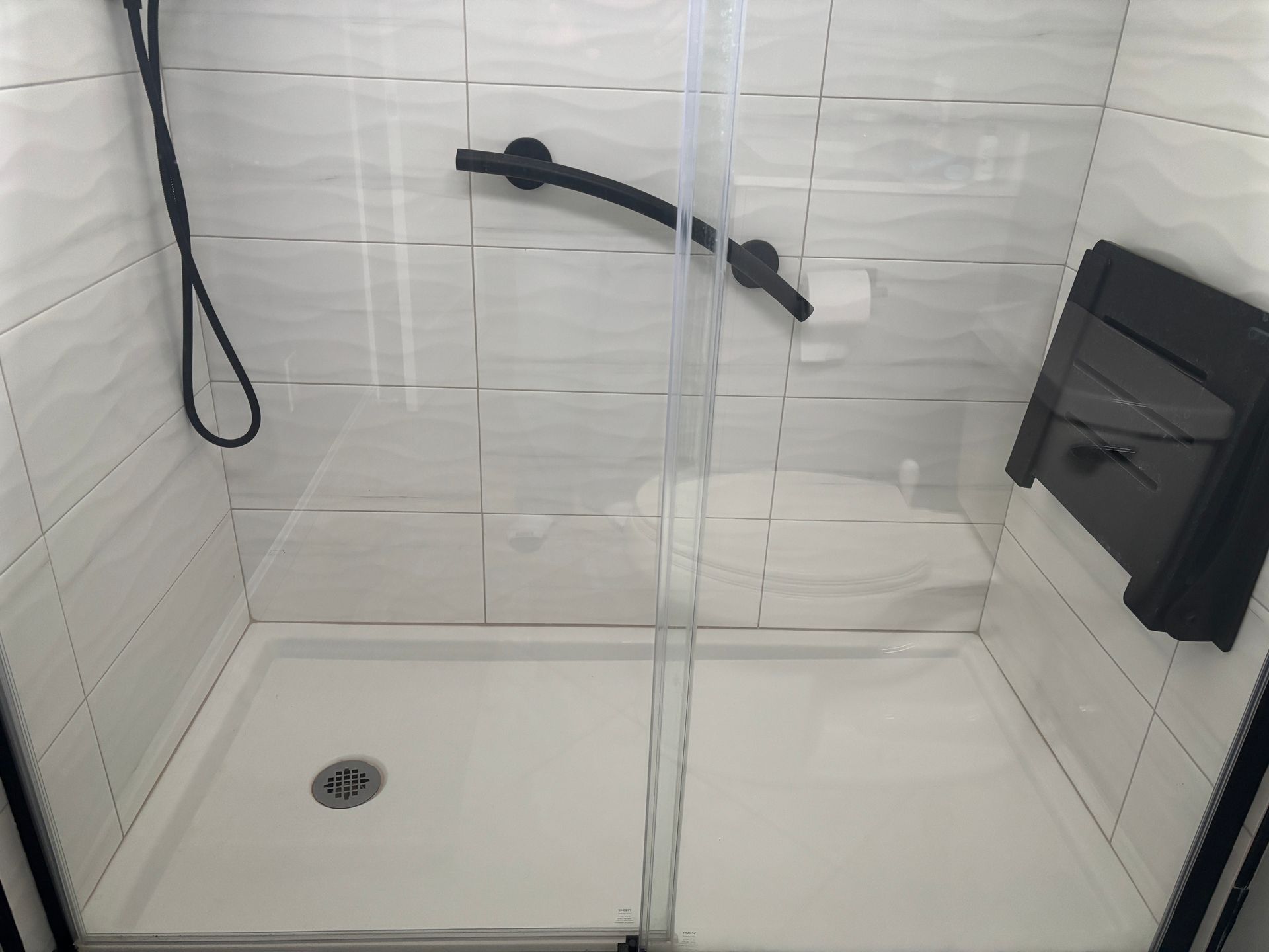 A shower stall with a black handle and a black shower head.