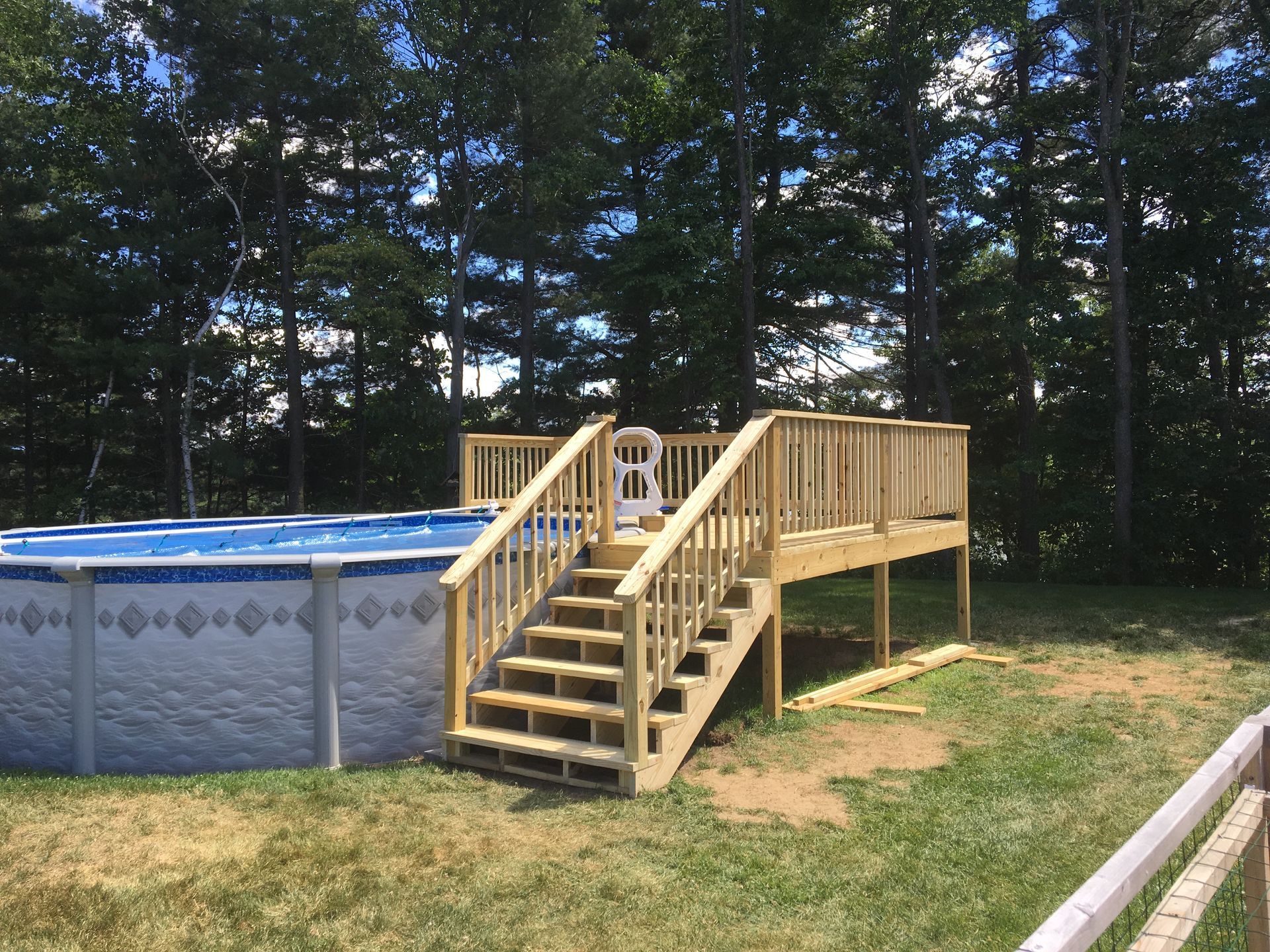 A swimming pool with a wooden deck and stairs surrounded by trees.
