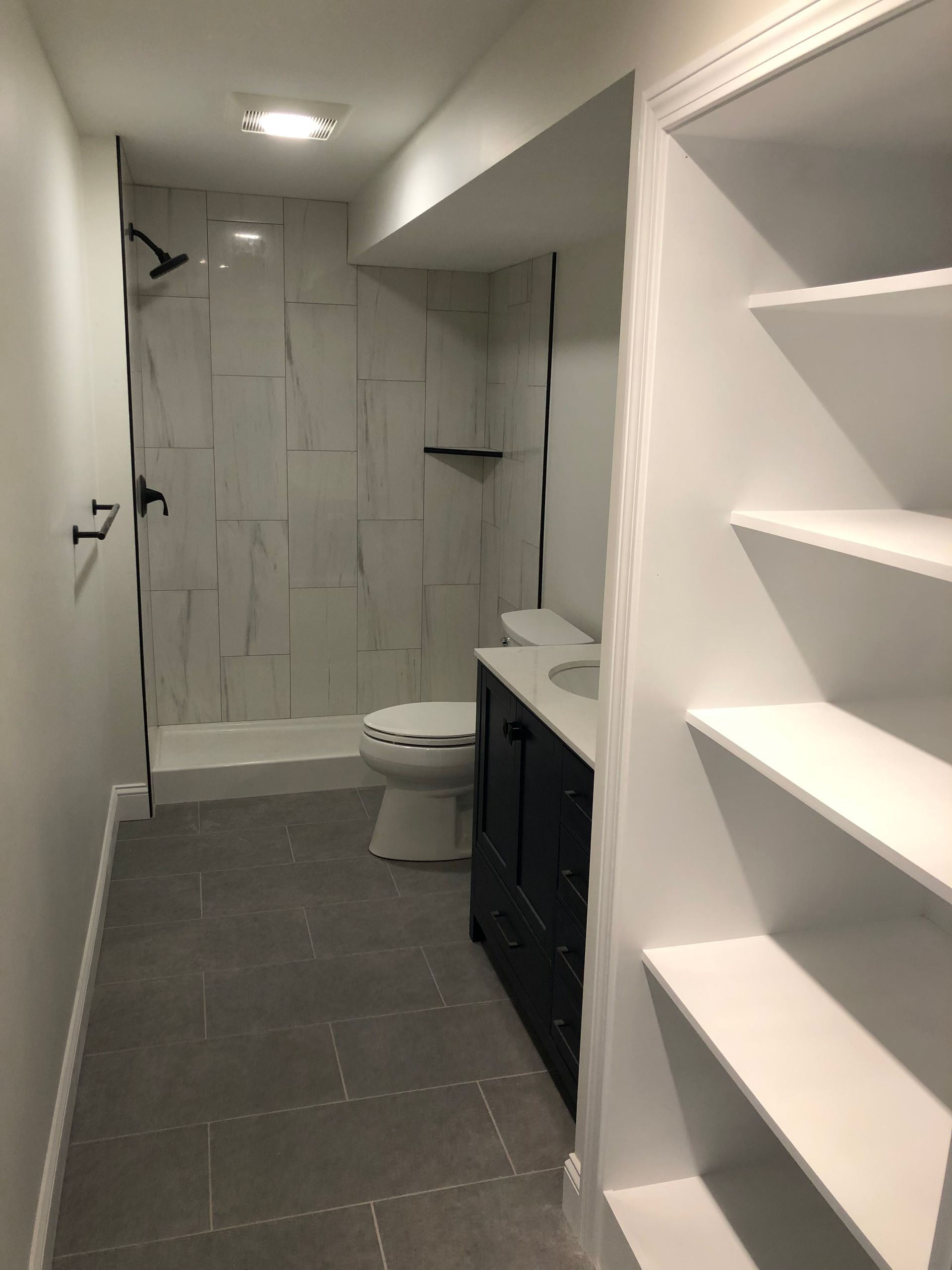 A bathroom with a toilet , sink , shower and shelves.