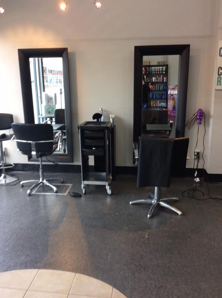 Hair salon interior with two black-framed mirrors, chairs, a cart, and dark floor.