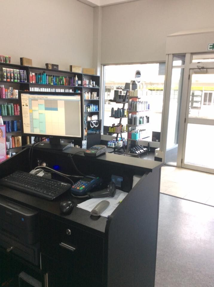 Reception desk in a shop, with a computer, products on shelves, and a doorway visible.