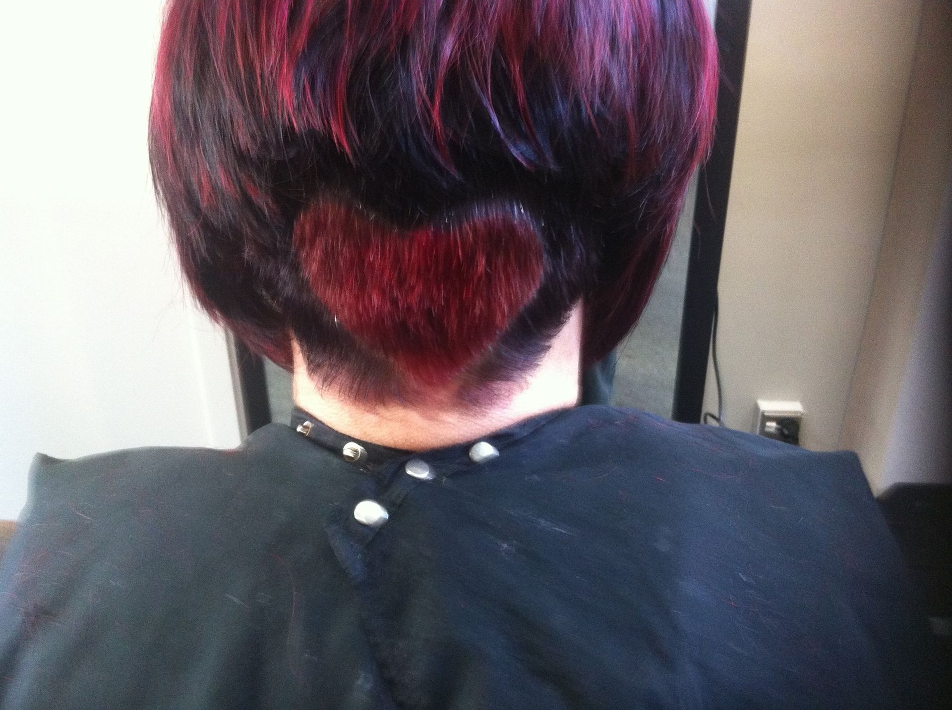 Woman with a dark bob haircut, shaved heart shape in the back, red highlights.