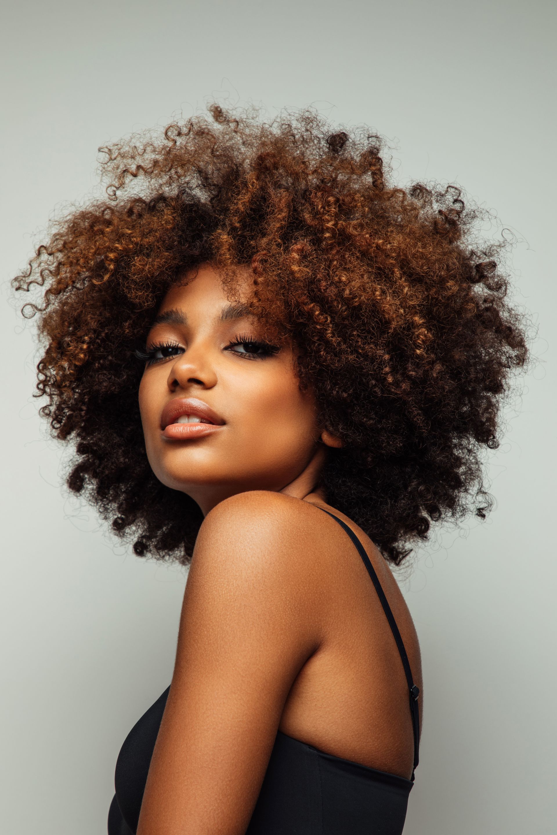 Woman with large afro looking over shoulder, dark skin, wearing black top.