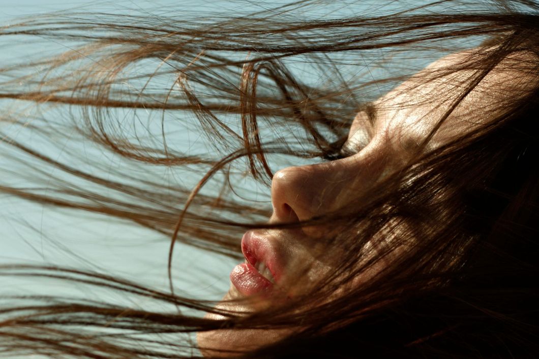 Woman with dark hair blowing in the wind, eyes closed, outdoors.