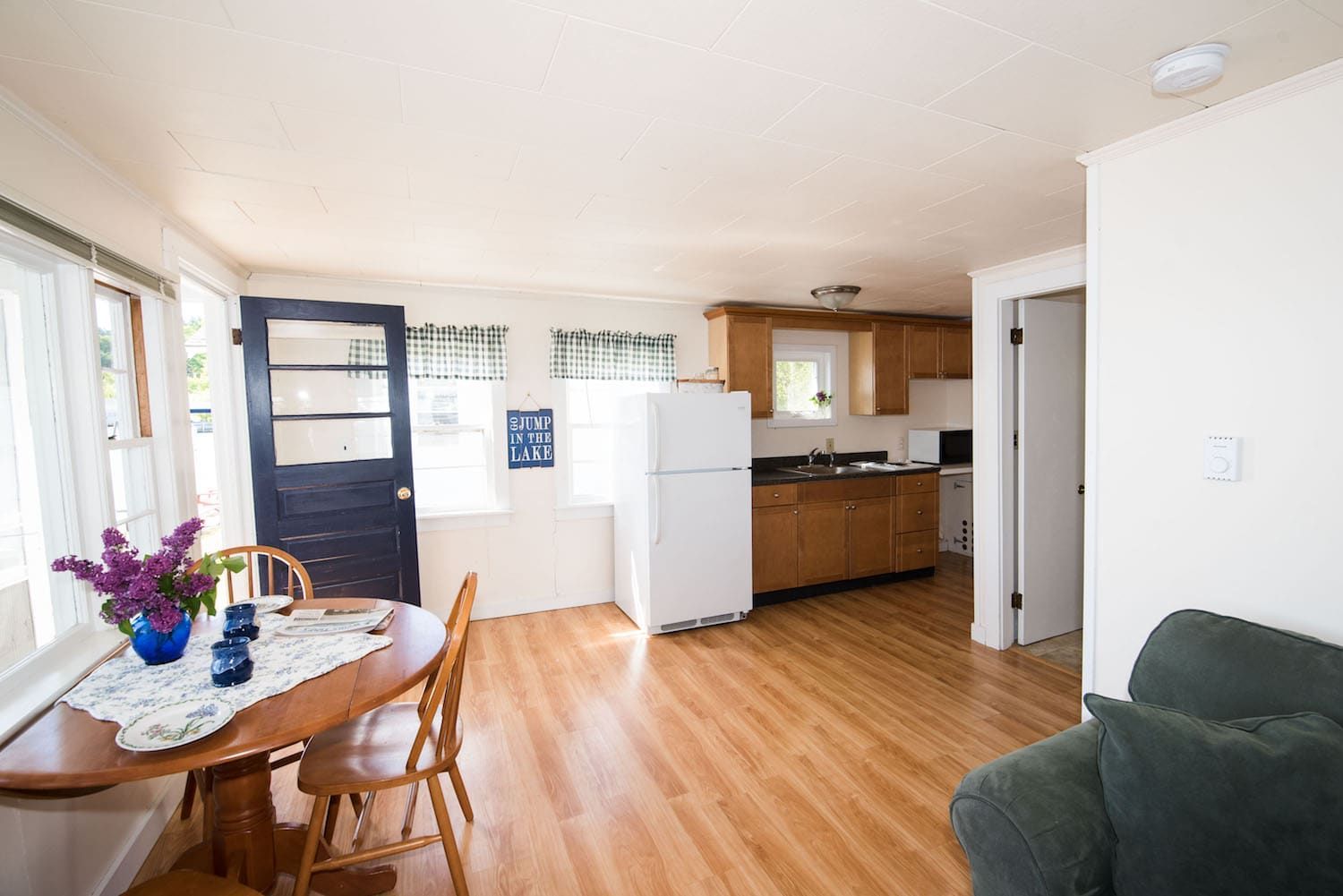 A living room with a table and chairs and a kitchen with a refrigerator.