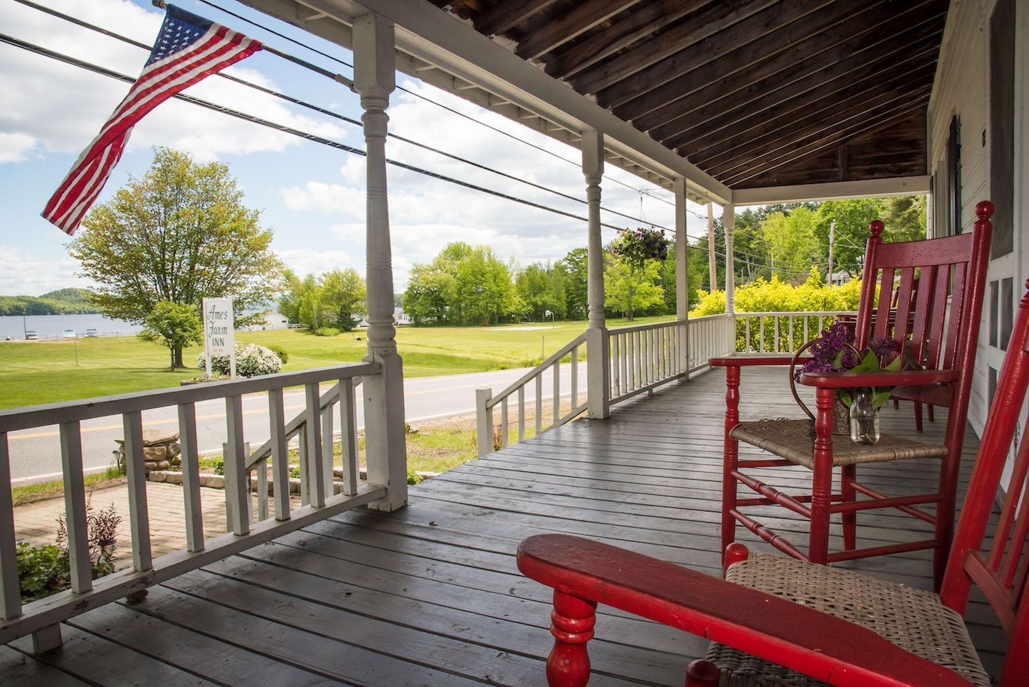 A porch with two red rocking chairs and an american flag.