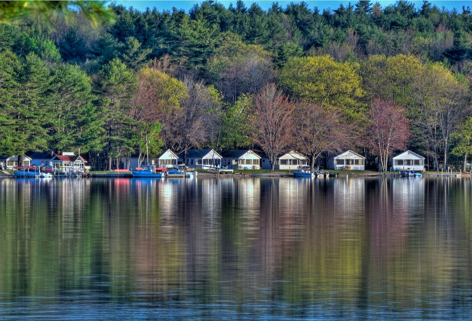 A row of houses sit on the shore of a lake surrounded by trees.