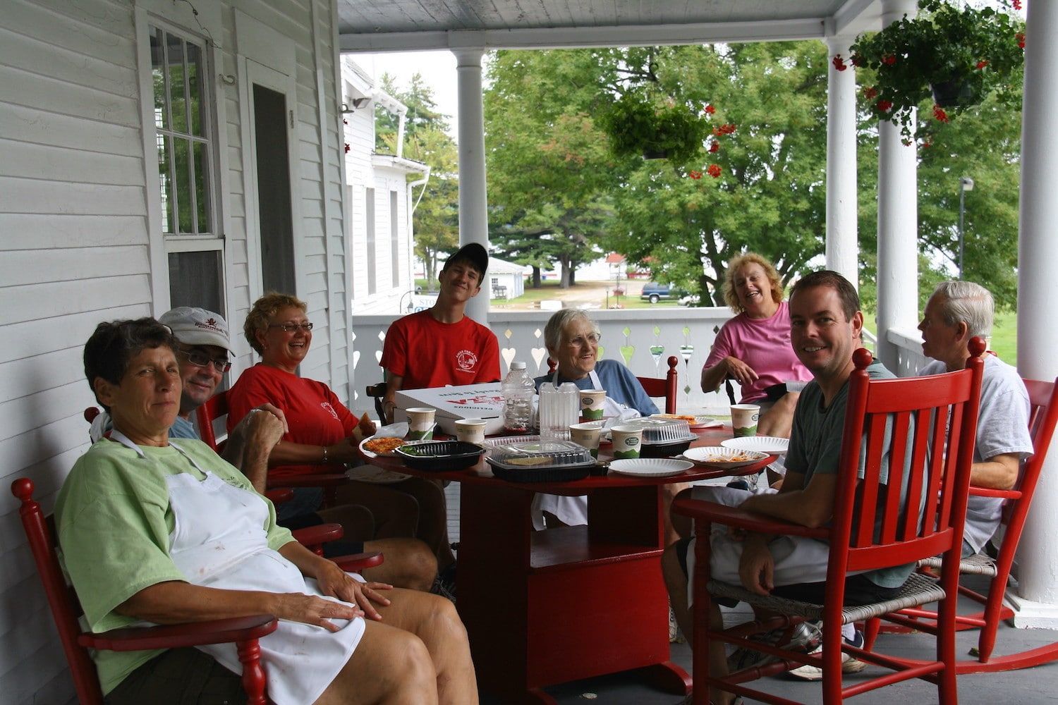 A group of people are sitting around a table on a porch.