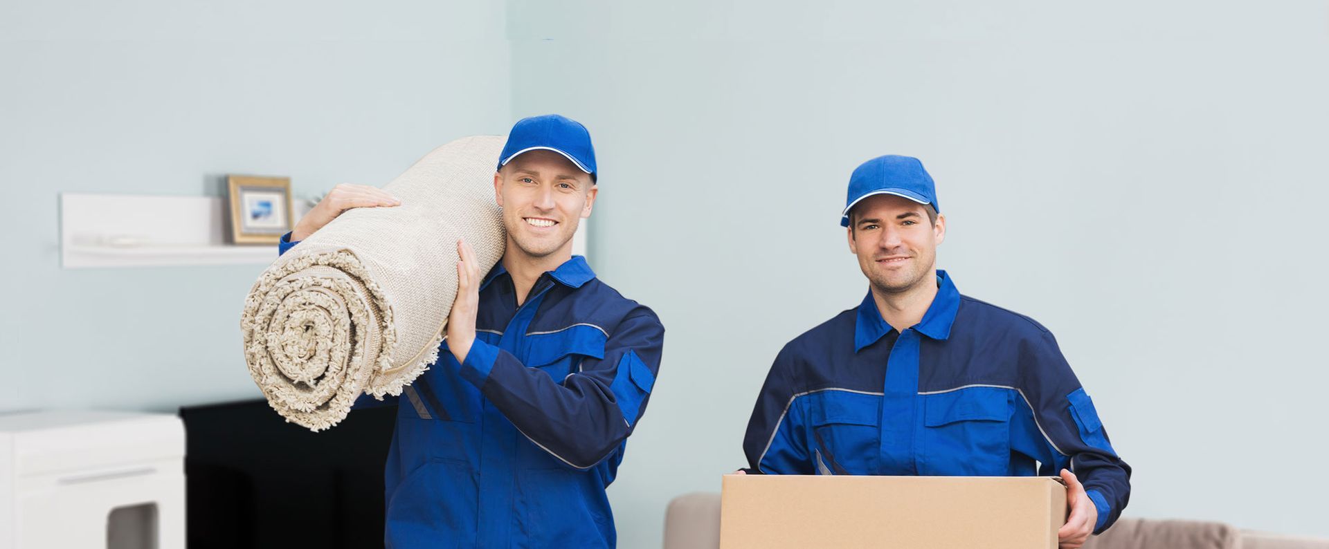 two movers are carrying a rug and a box in a living room