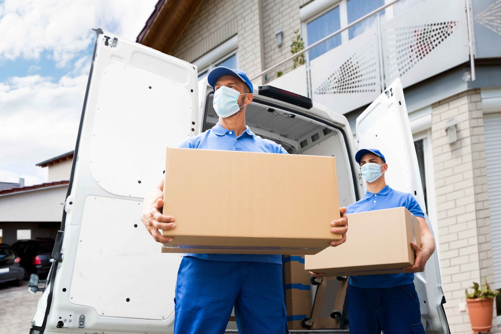 two delivery men wearing masks are carrying boxes out of a van