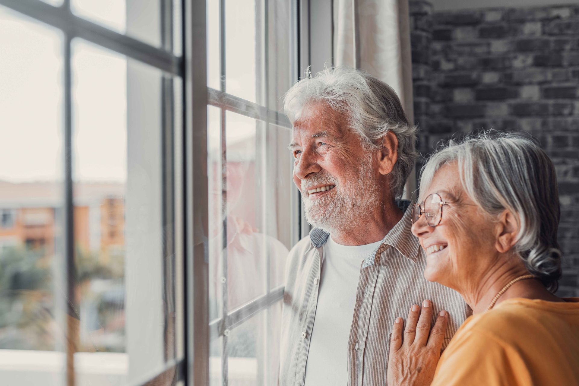 an elderly couple is looking out of a window