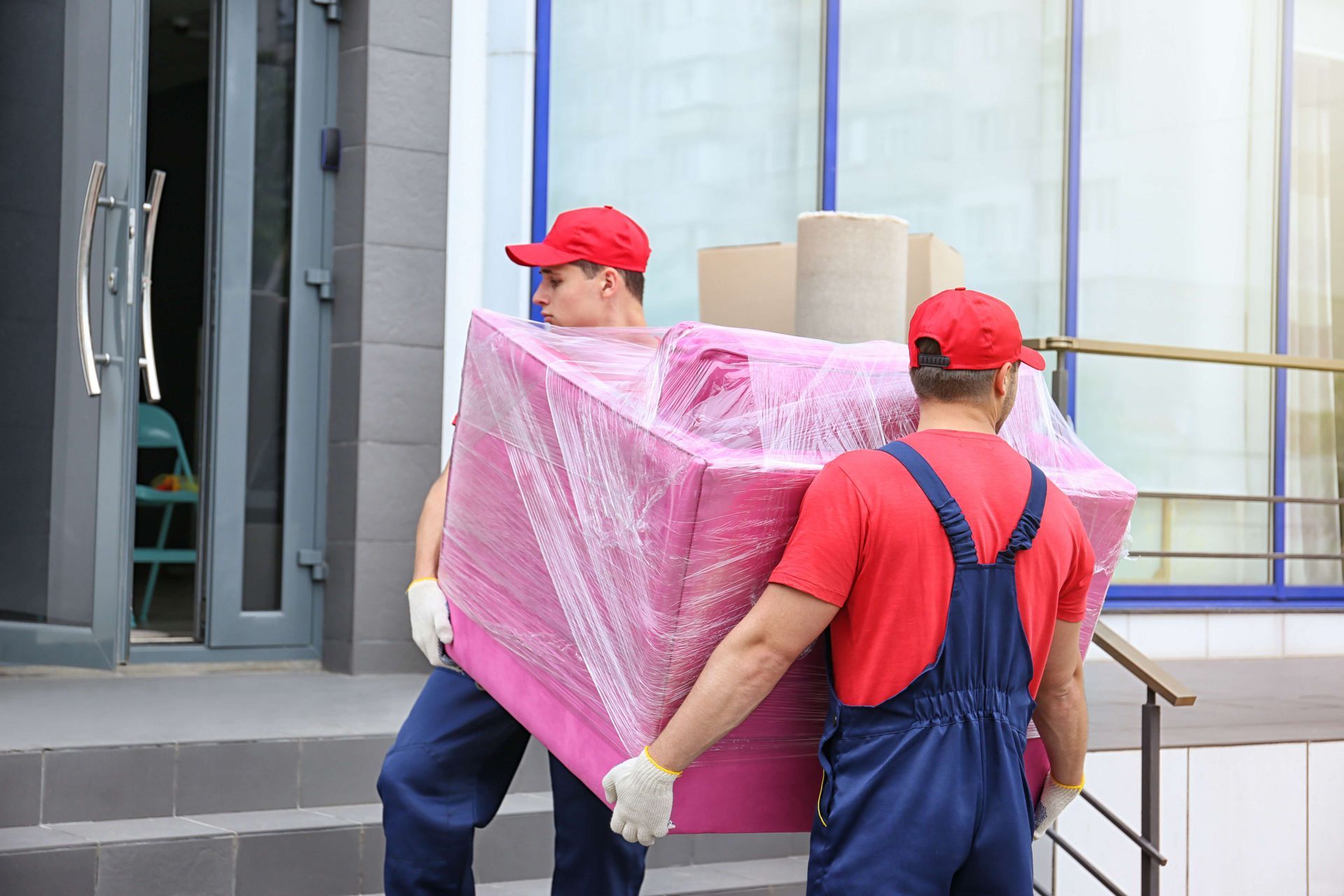 two men are carrying a large pink box on their backs