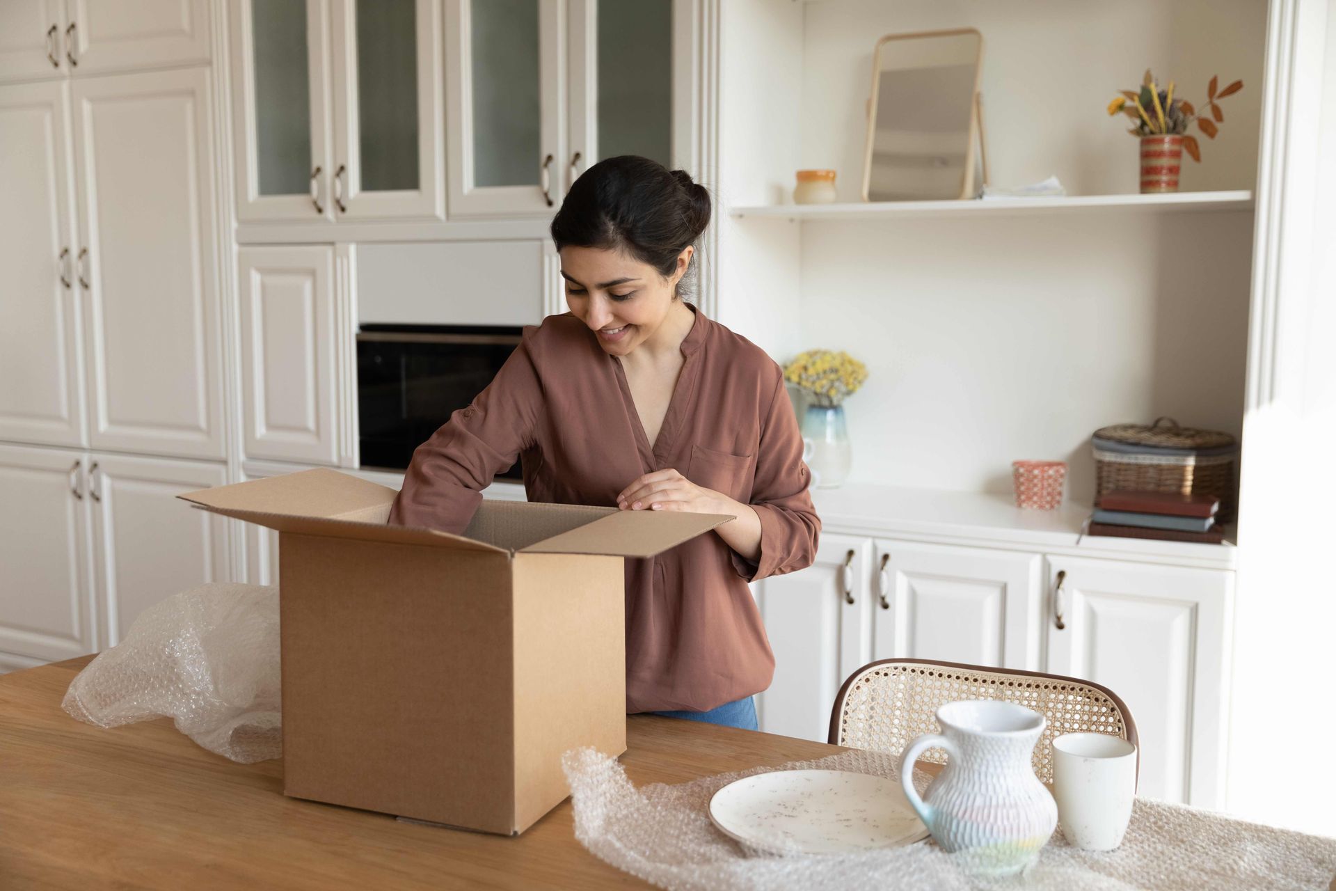 a woman is opening a cardboard box in a kitchen