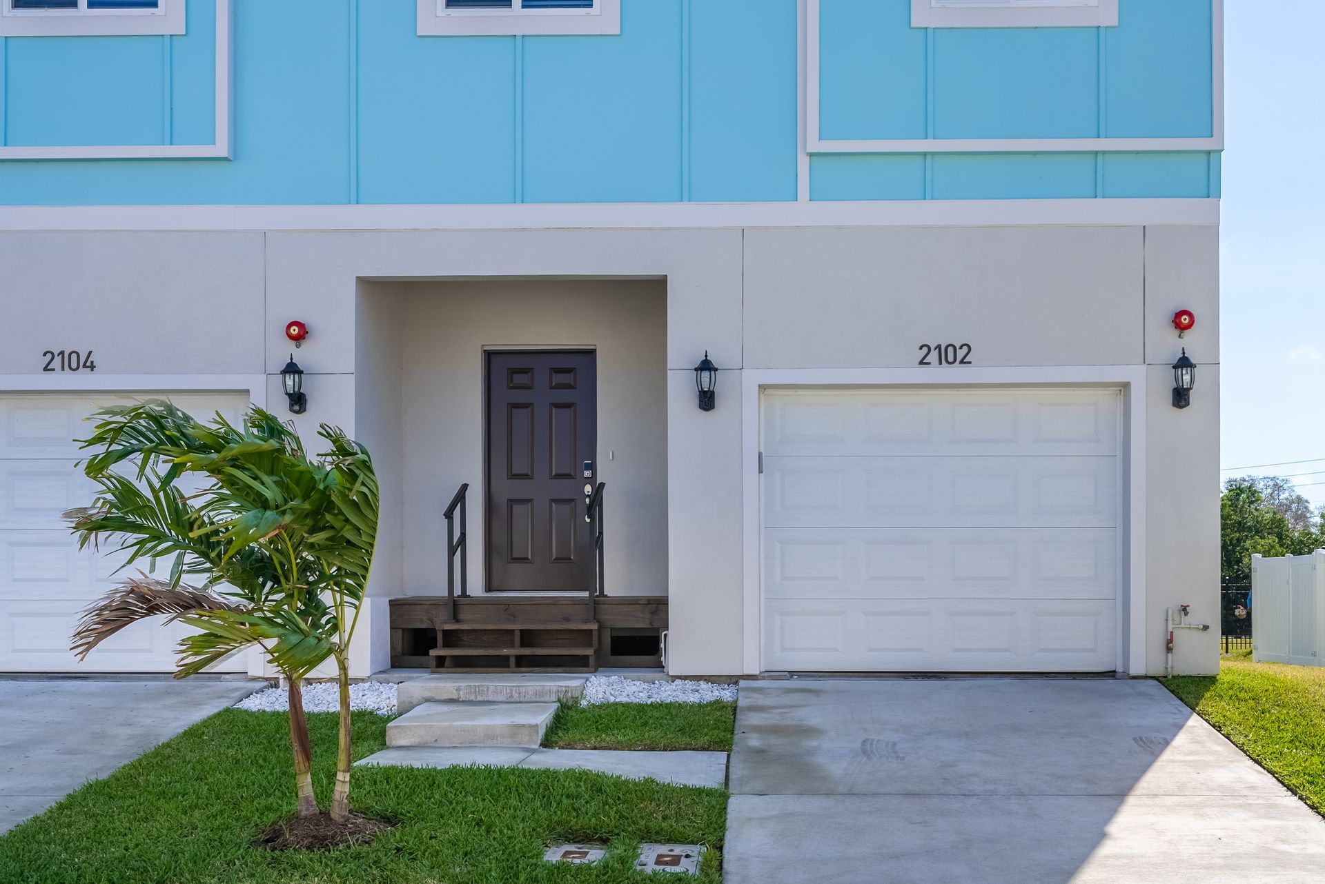 a blue and white house with two garages and a palm tree in front of it at Whitney Place Apartments in Clearwater, FL.