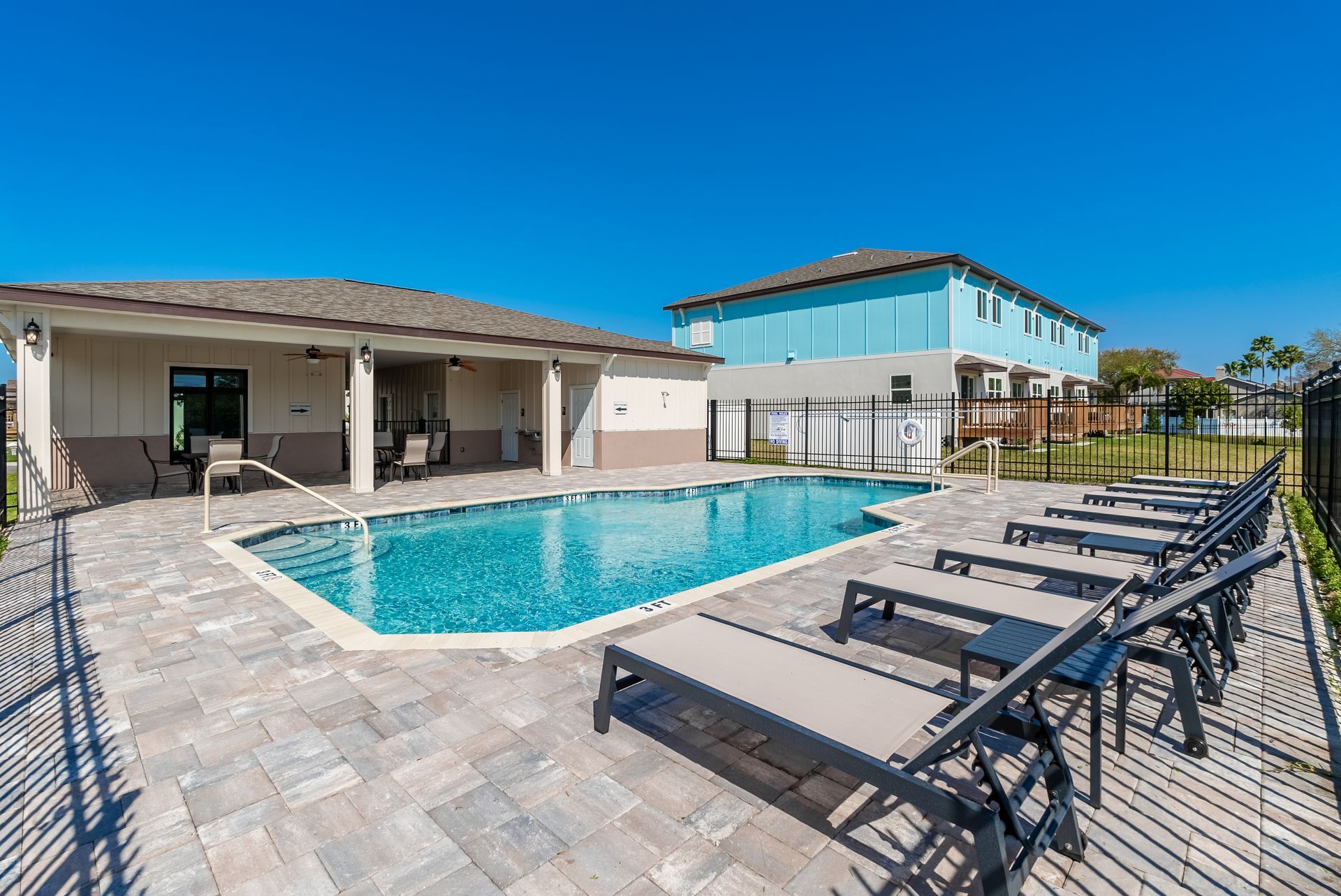 a large swimming pool surrounded by lounge chairs in front of a house at Whitney Place Apartments in Clearwater, FL.