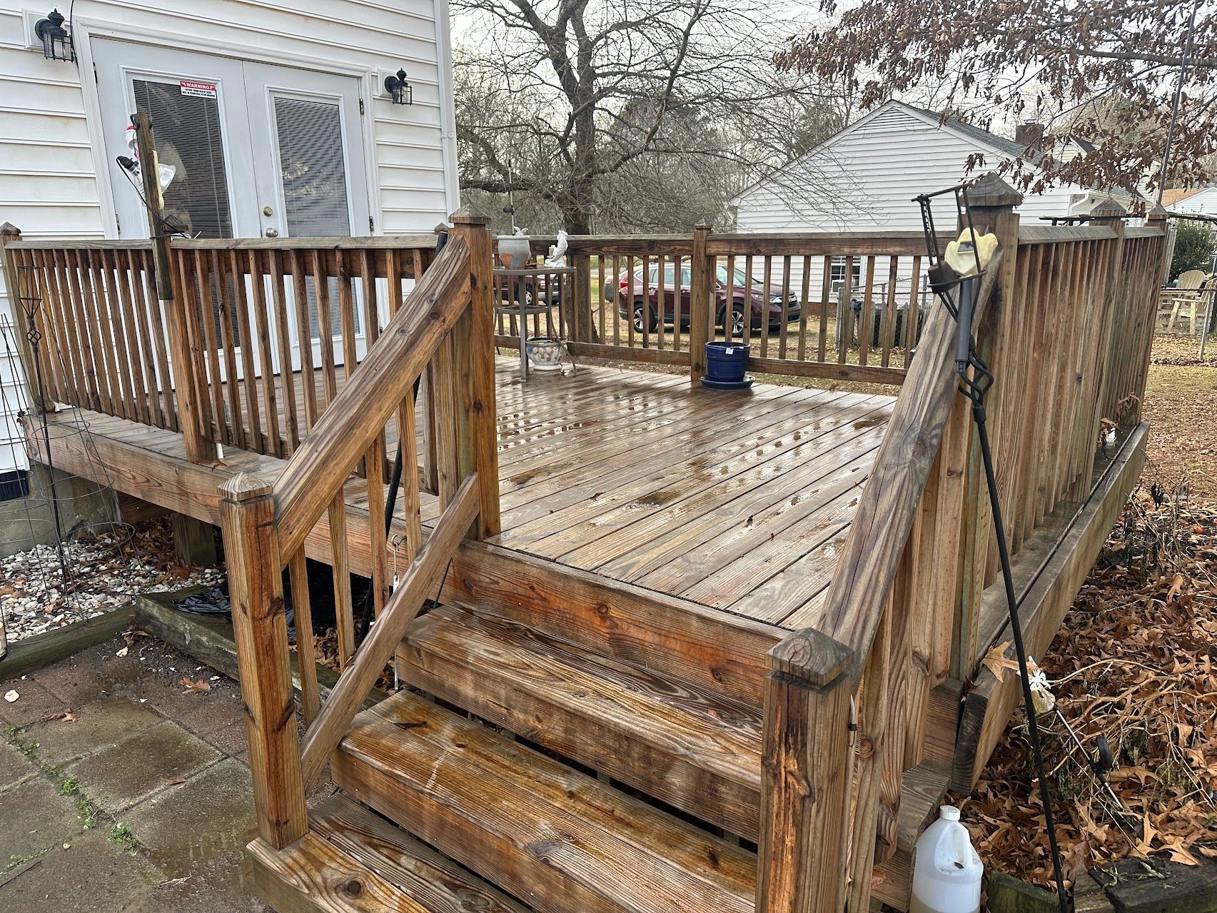 A wooden deck with stairs leading up to it and a white house in the background.