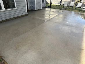 A concrete patio with chairs and tables in front of a house.