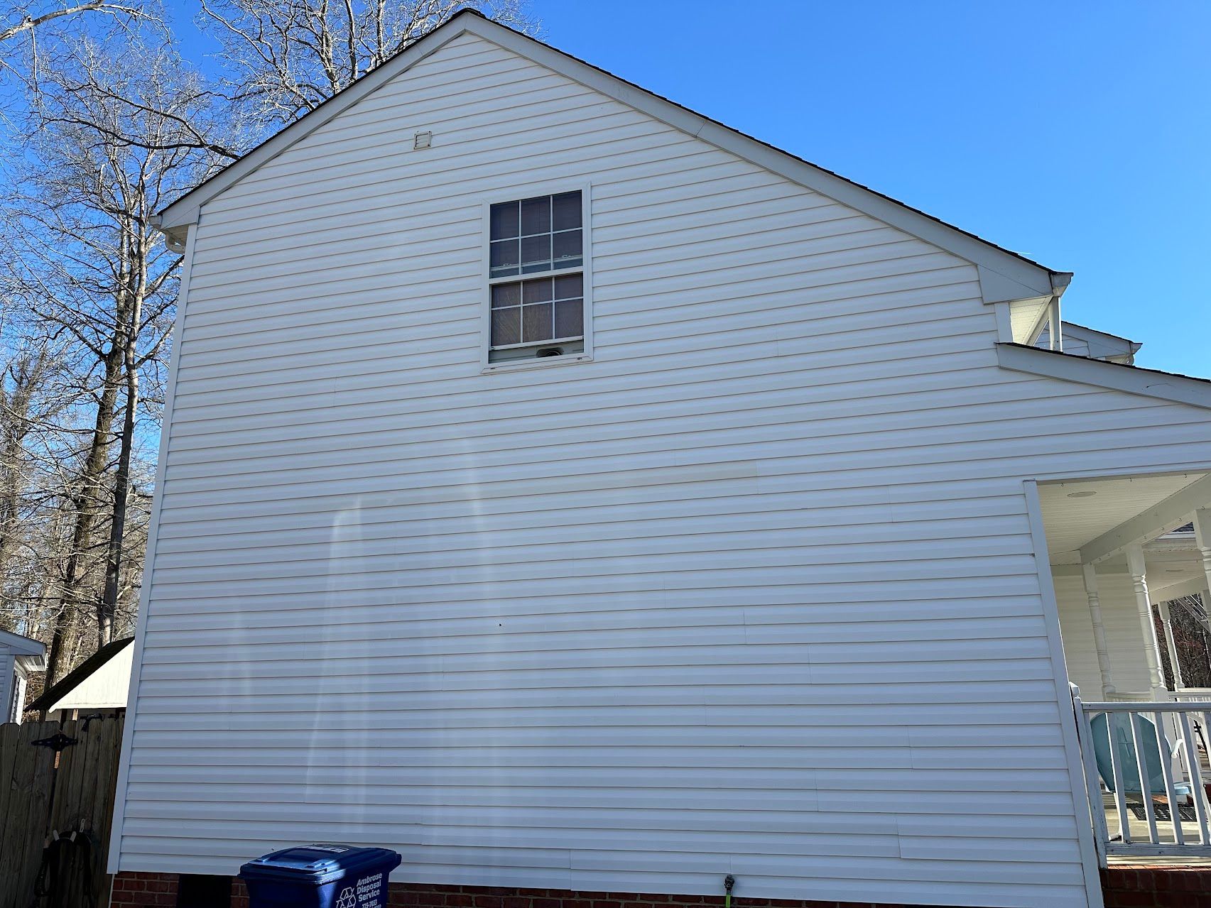 A white house with a blue trash can in front of it.