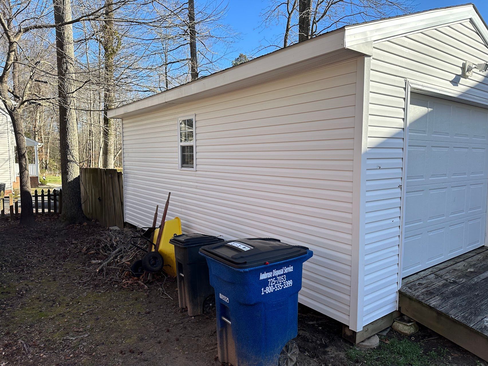 A white shed with blue trash cans in front of it.