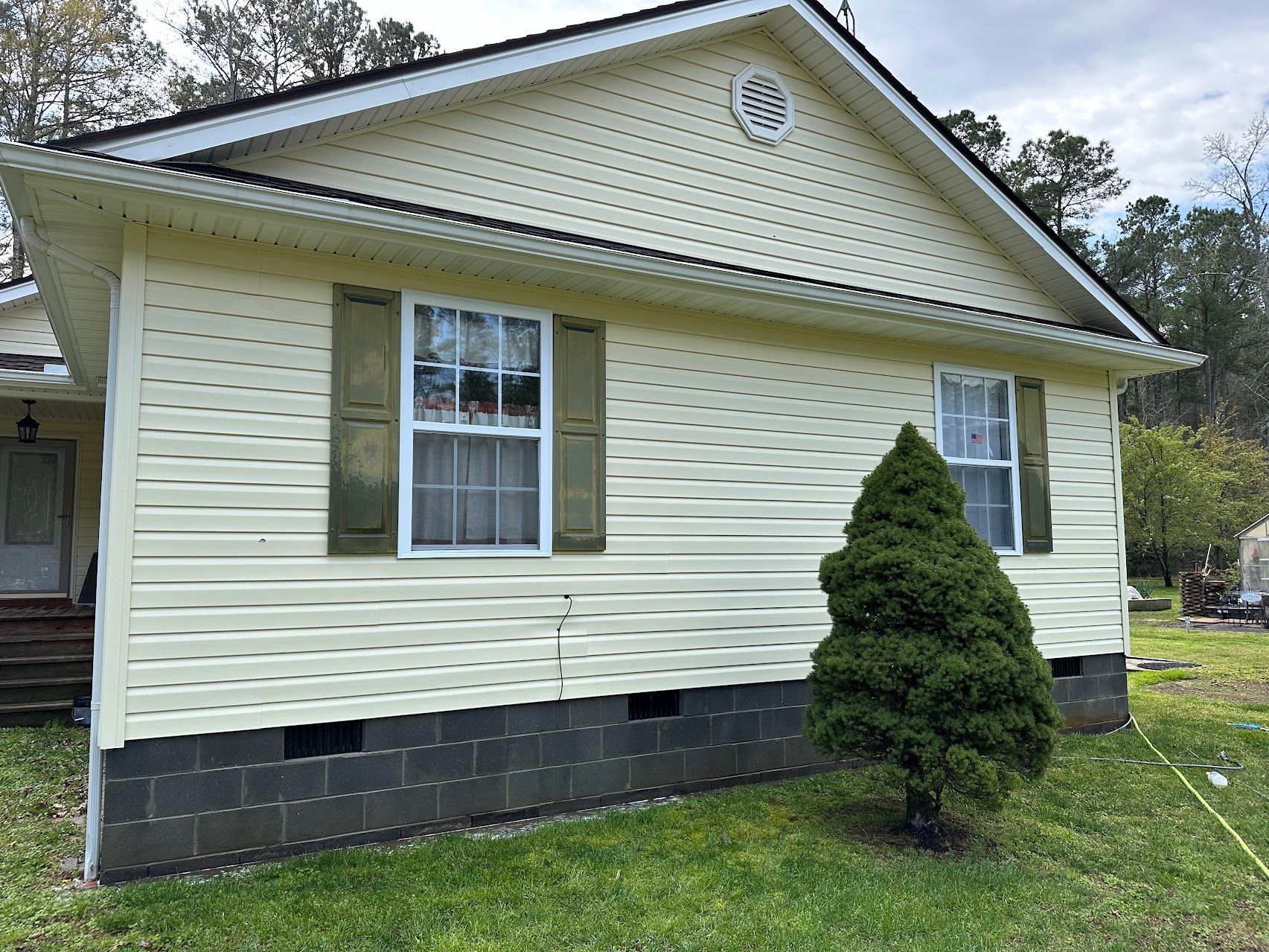 A white house with green shutters and a christmas tree in front of it.