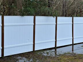 A white fence with wooden posts is surrounded by trees and a puddle of water.