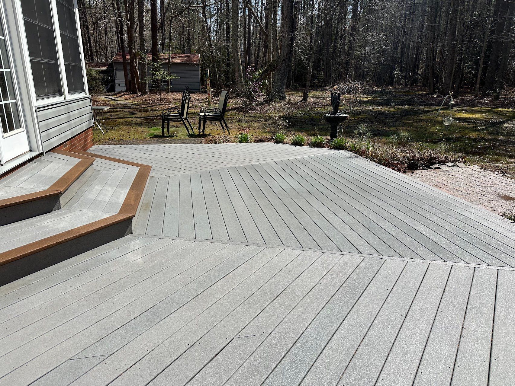 A wooden deck with stairs and a screened in porch in the background.