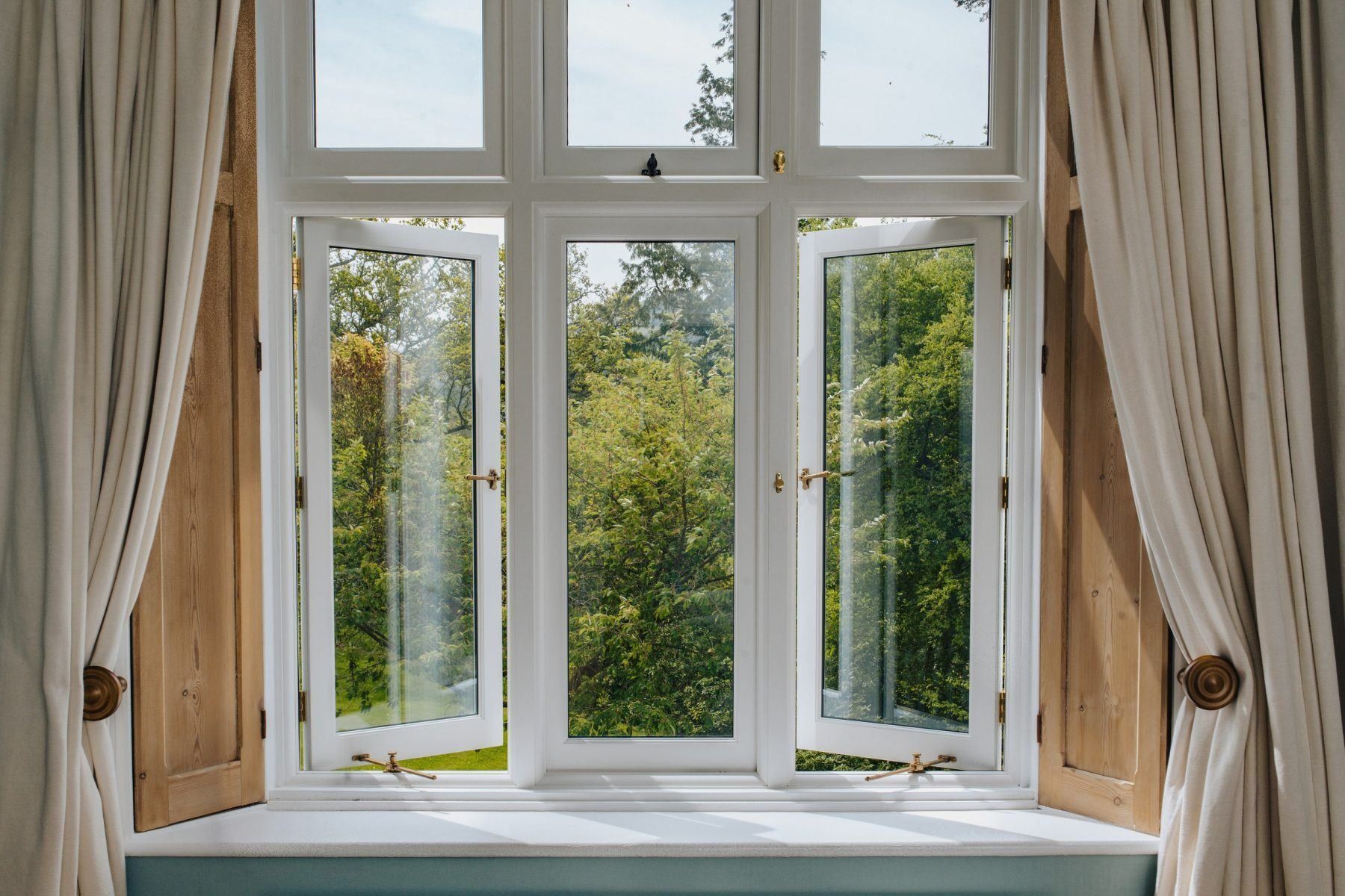Open white framed window with two opened panels, green trees visible through glass. Cream curtains frame the window  — Local Glassmaster in Huskisson, NSW