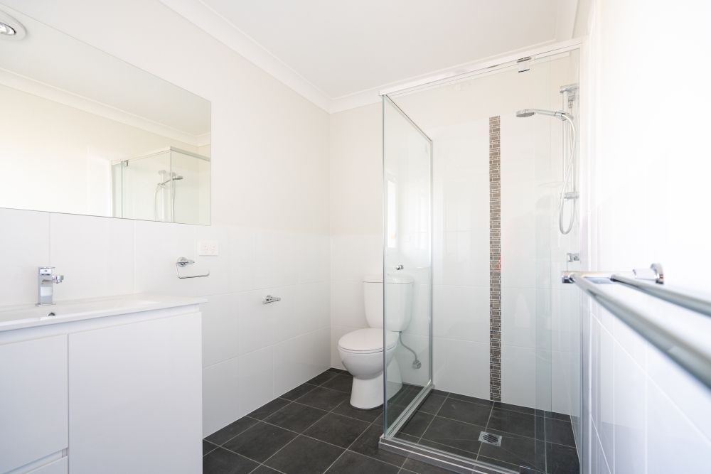 White Bathroom With Dark Tile Floor With Glass Shower — Local Glassmaster in Huskisson, NSW