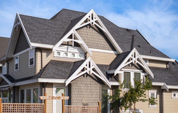 Large beige house with dark gray roof and white trim under a blue sky