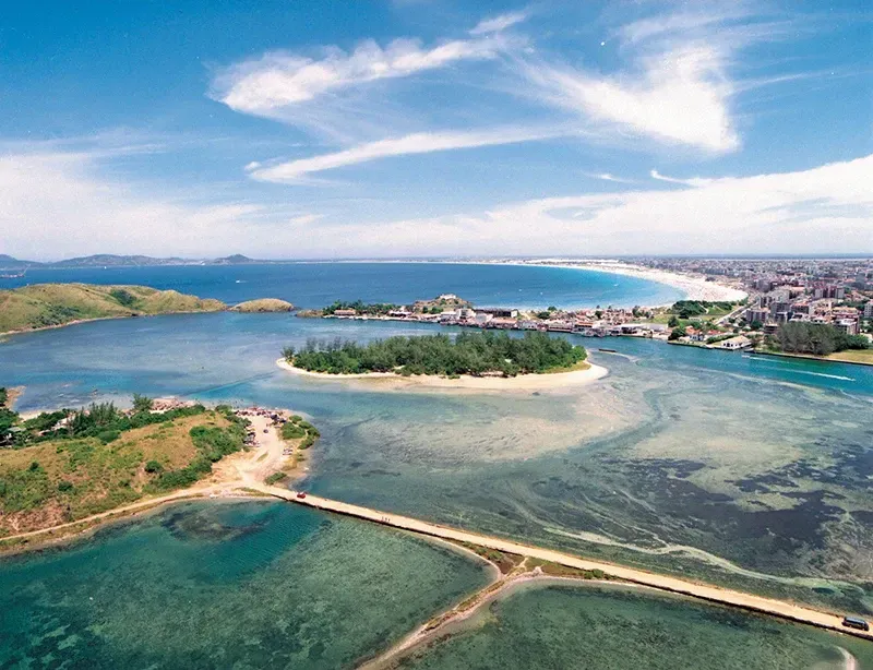 Vista aérea de uma cidade costeira com ilhas, água turquesa, céu azul e uma ponte.