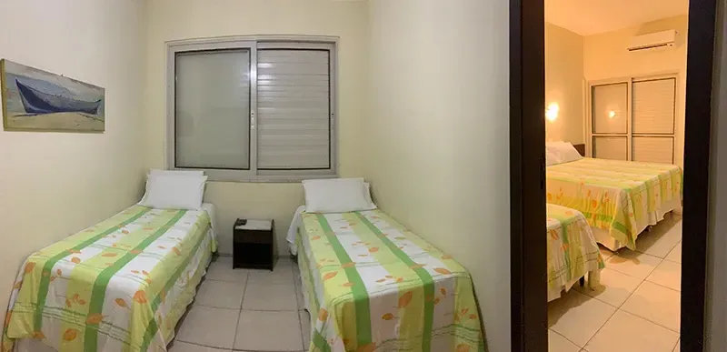 Dois quartos com camas de solteiro e um quadro. Outro quarto com uma cama é visível através de uma porta.