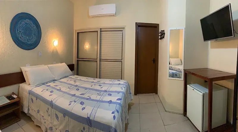 Quarto com cama, mesinha com espaço para laptop, banco curvo embutido e janela.