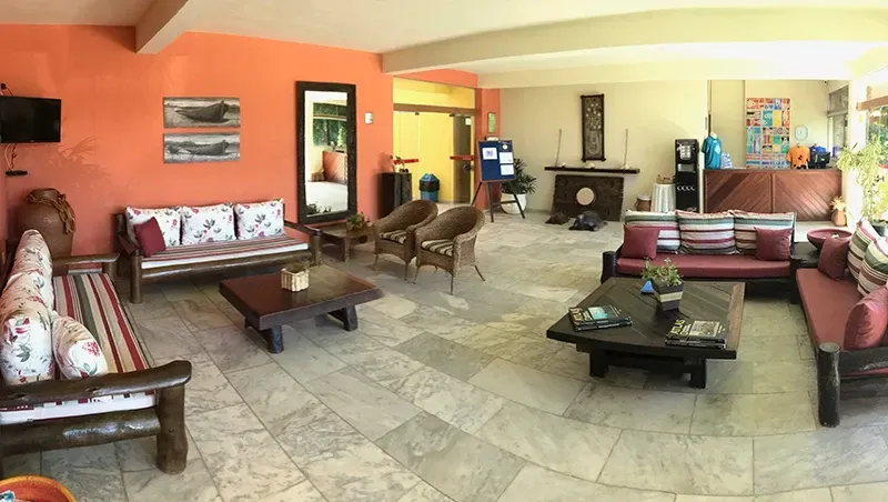 Sala de estar com parede laranja, móveis de madeira e piso de mármore. Sofás com almofadas florais e listradas.