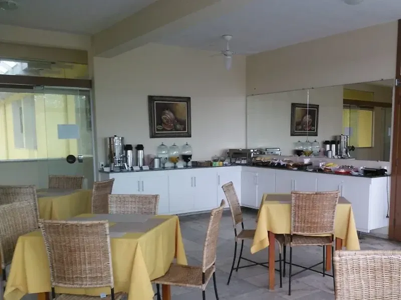 Buffet de café da manhã em uma sala ensolarada com mesas postas para os clientes.