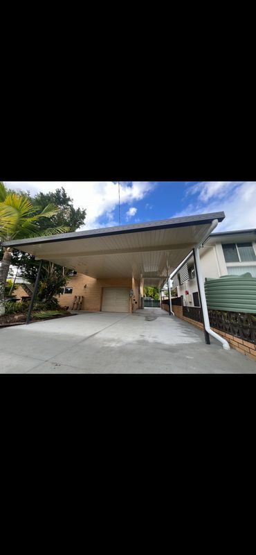 Carport attached to a house with concrete driveway, blue sky.