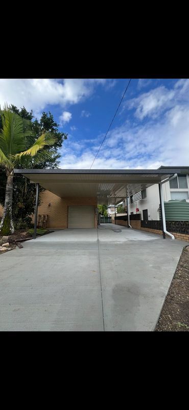 Concrete driveway leading to a carport, with a clear sky above.