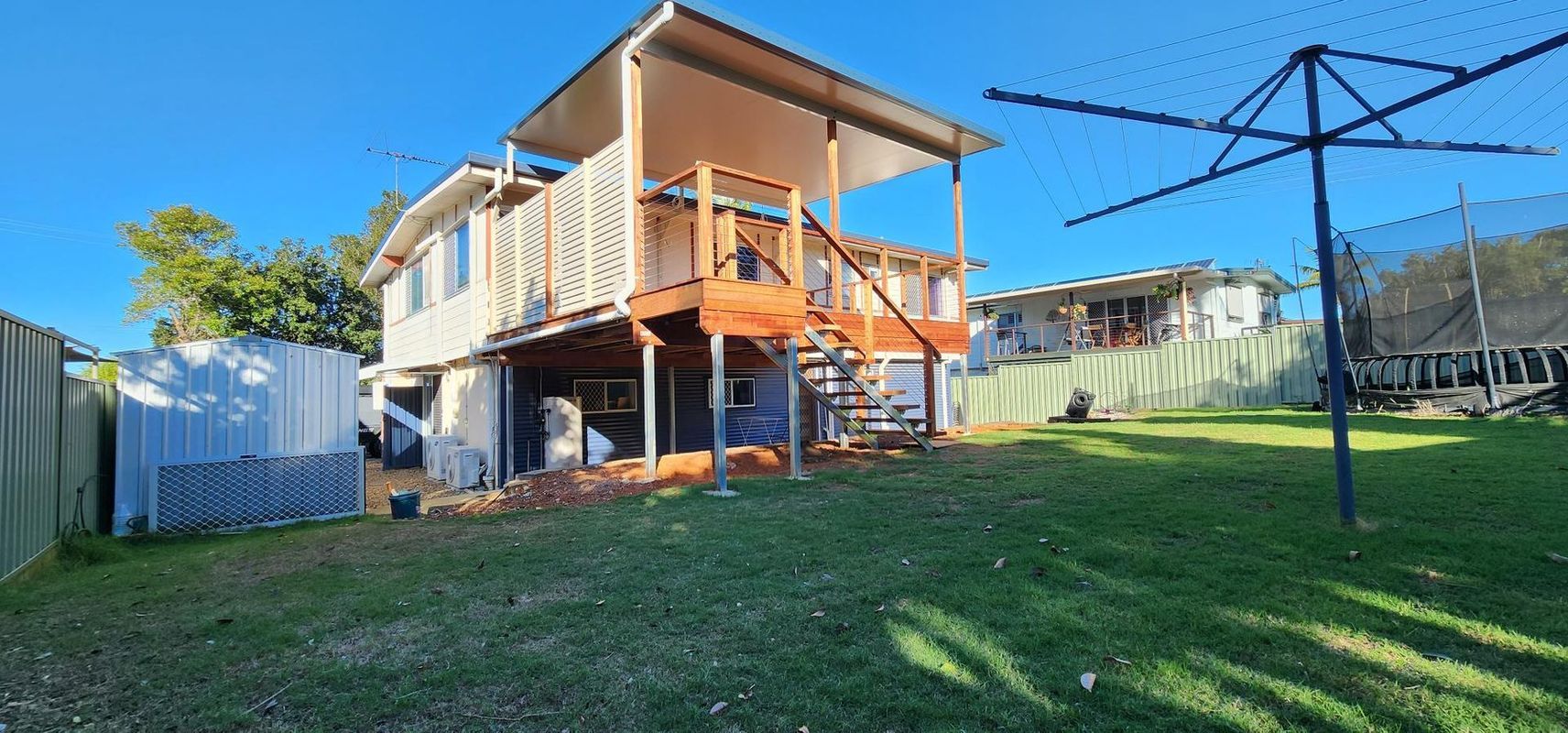 Two-story house with a wooden deck and staircase. A clothesline is in the backyard.