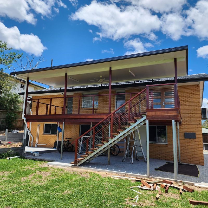 Two-story brick house with wooden deck and staircase, blue sky.