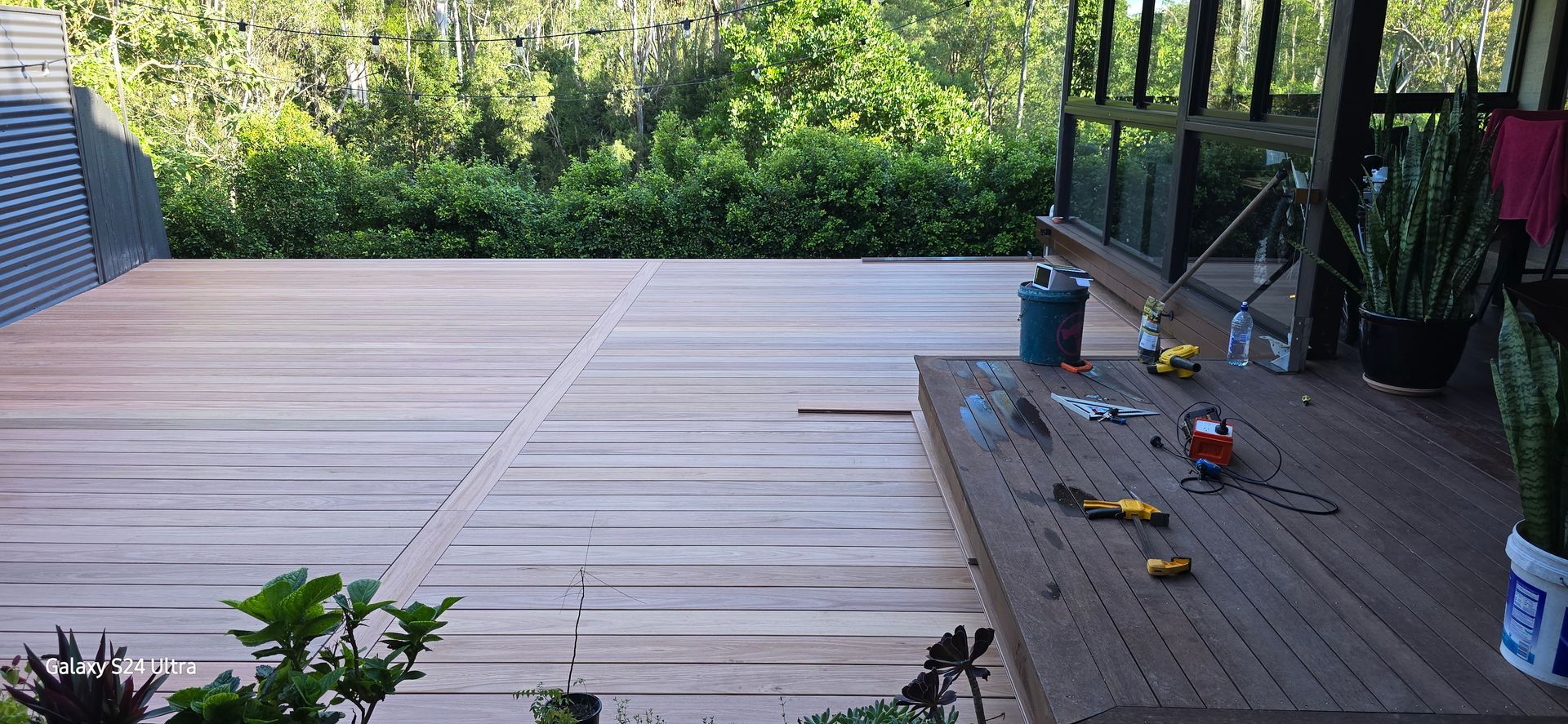 Wooden deck with tools and plants overlooking greenery.