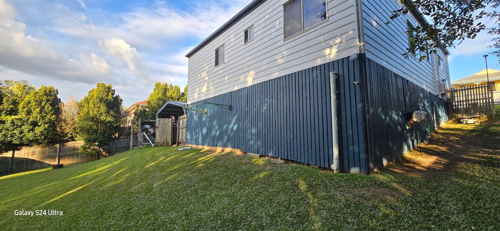 Side view of a building with blue siding and a green lawn. Trees and a cloudy sky in the background.