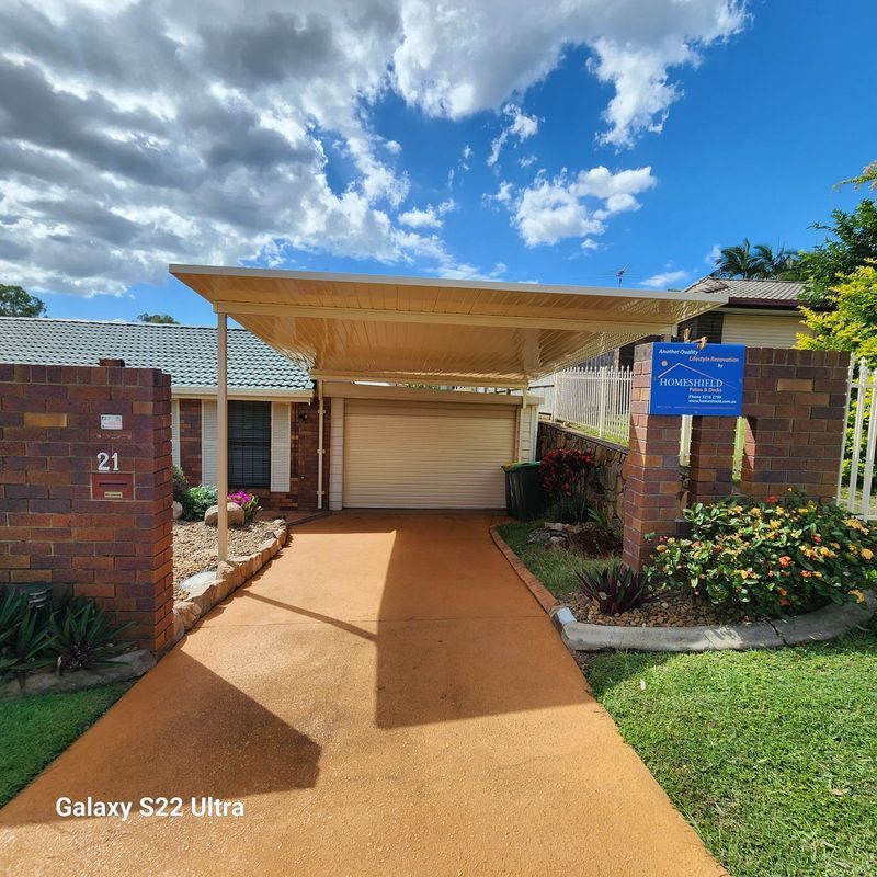 A residential house with a carport and driveway. Brickwork and a sign. Cloudy sky.